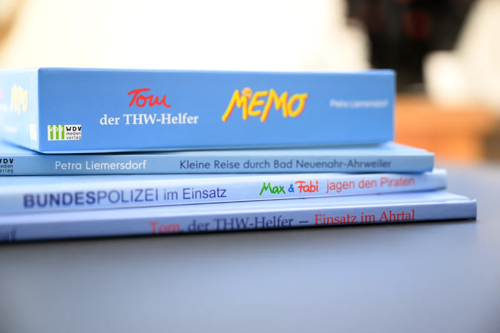 2025_Warlich_Druck_Meckenheim_August_JR_02362 Kopie Buchrücken mehrerer Bücher von Tom, der THW-Helfer und die Seitenansicht eines Memory-Spiels