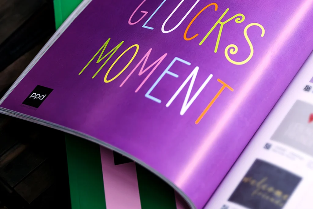 Gluecksmoment Aufgeschlagene Katalogseiten mit dem bunten Schriftzug „Glücksmomente“